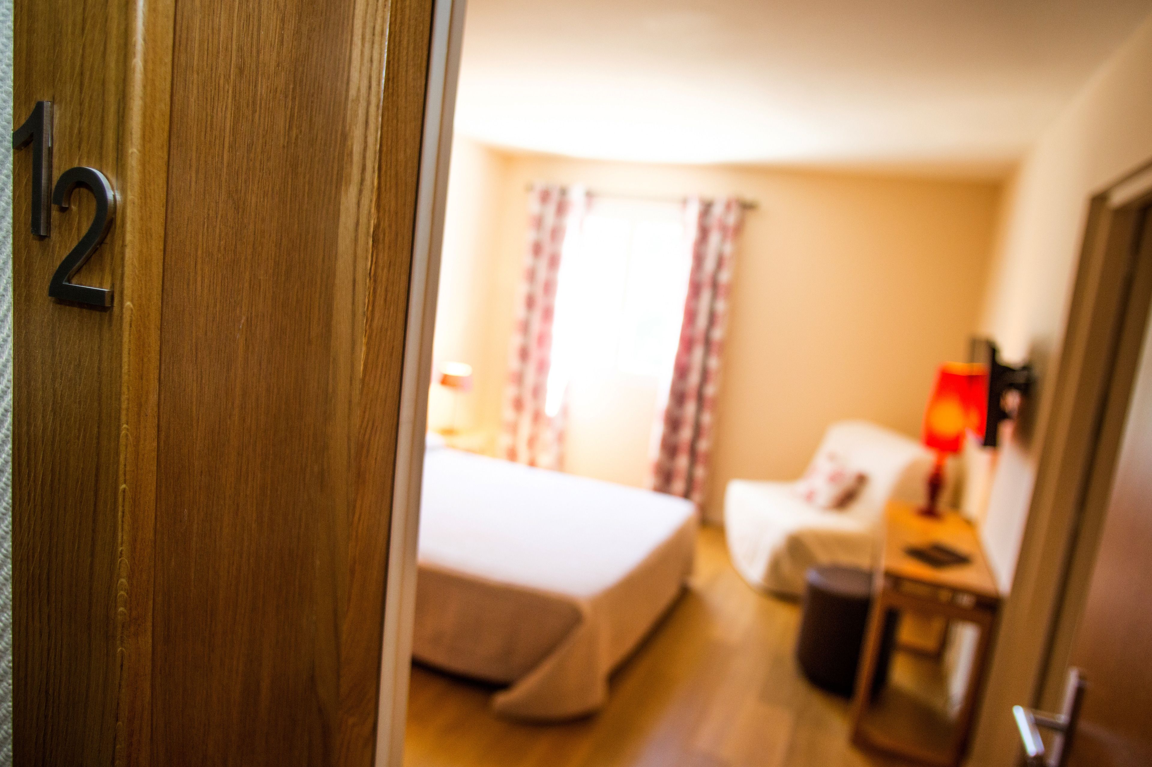 Une chambre d’hôtel avec un lit, une chaise, une table de chevet et des rideaux.