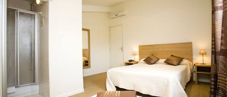 A hotel room with two beds, a shower, and a nightstand with a lamp.