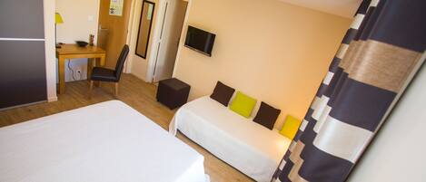 A hotel room with two beds, a desk, a chair, a TV, and a door.