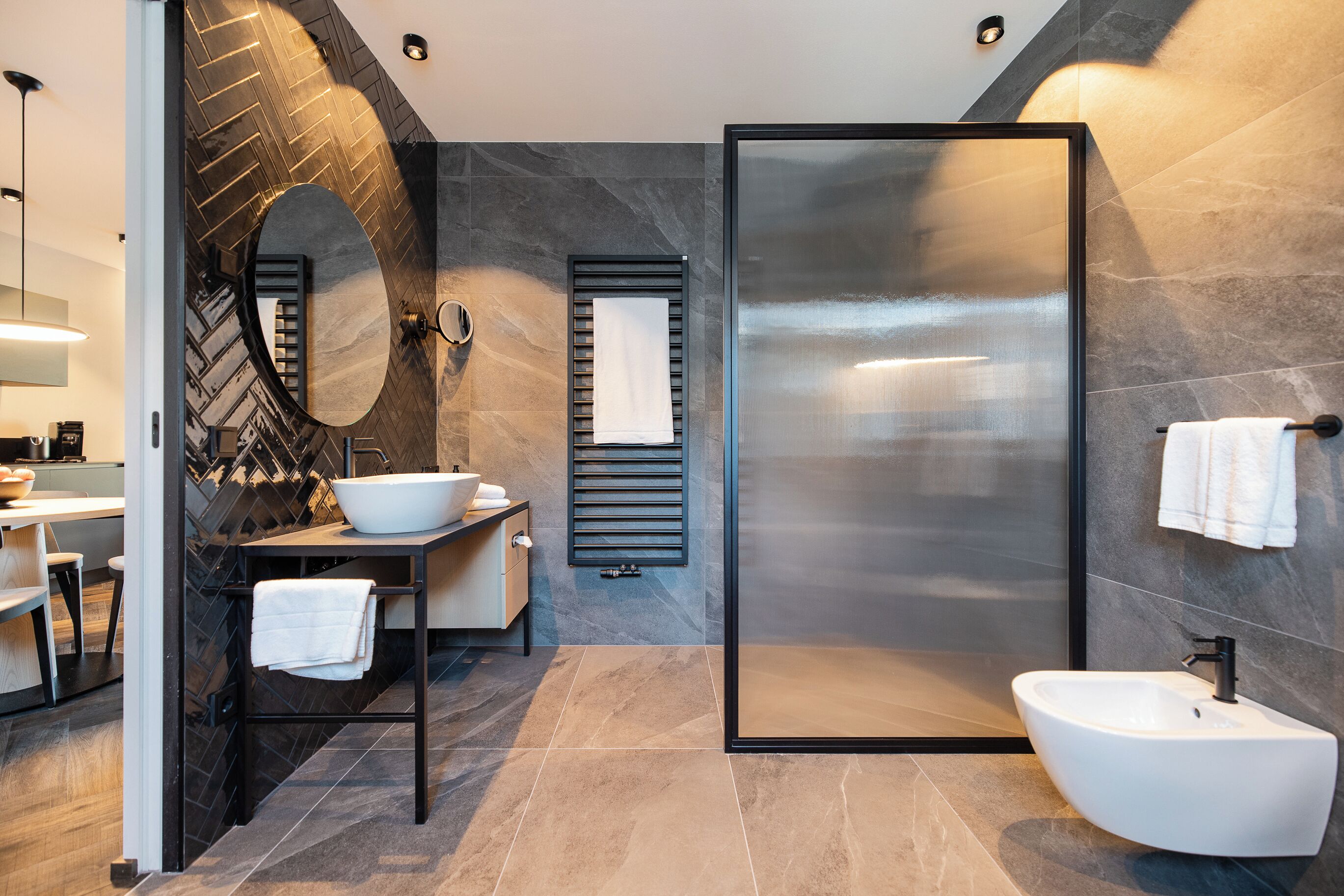 A modern bathroom with a large mirror, a freestanding sink, a glass shower enclosure, and a towel rack.