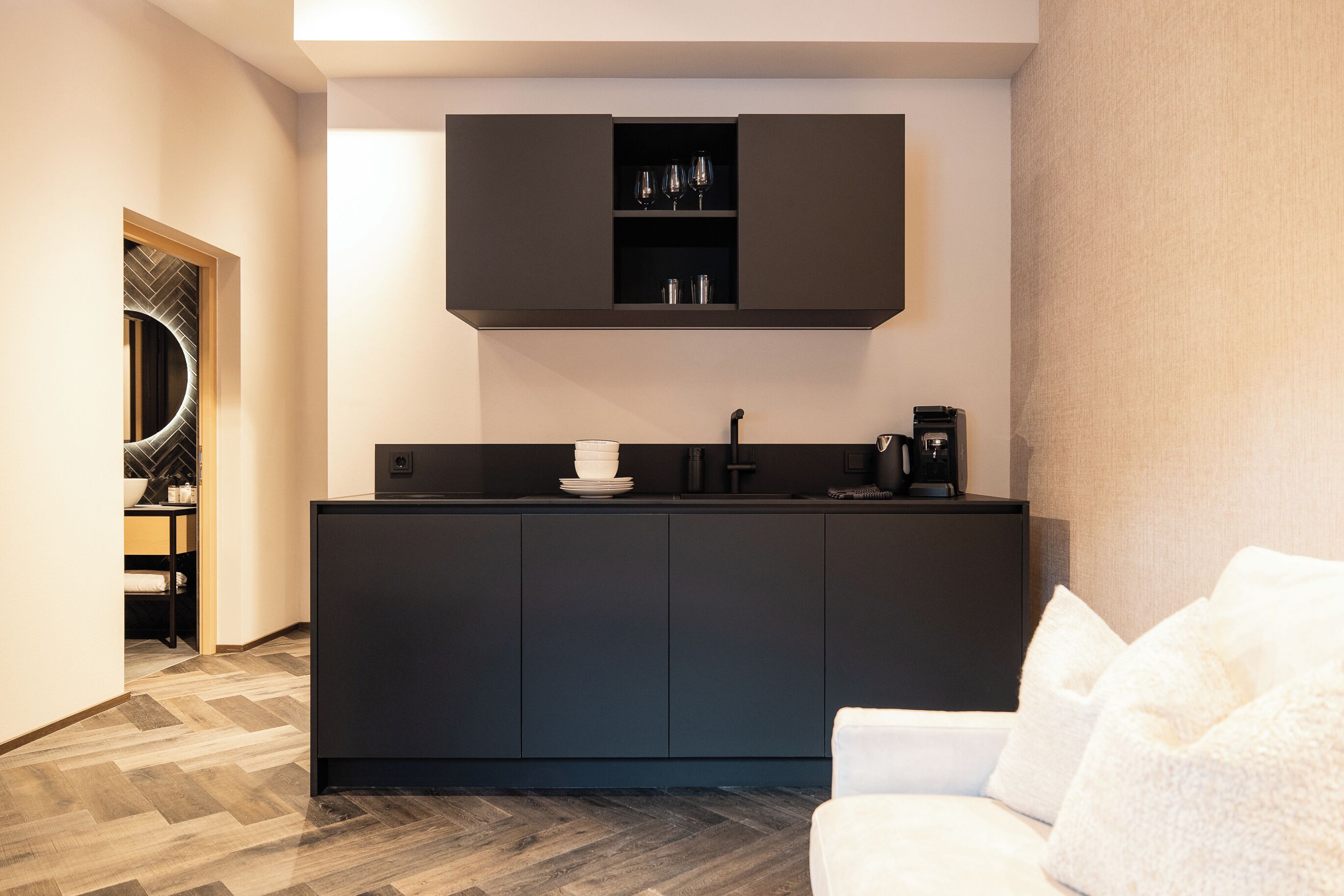 A modern kitchen with dark cabinetry, a built-in coffee machine, and a herringbone-patterned floor.