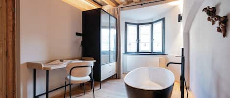 A modern bathroom with a freestanding bathtub, a wooden floor, and a window providing natural light.