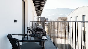 Un balcon avec un chat noir, une table avec une théière et une tasse, et une vue sur les montagnes.