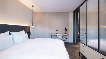 A modern hotel room with a large bed, a desk, and a wardrobe.