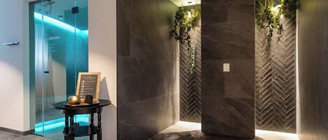 A modern lobby with a glass door, dark marble walls, and a herringbone-patterned wall. There is a small table with a framed sign and a cup.