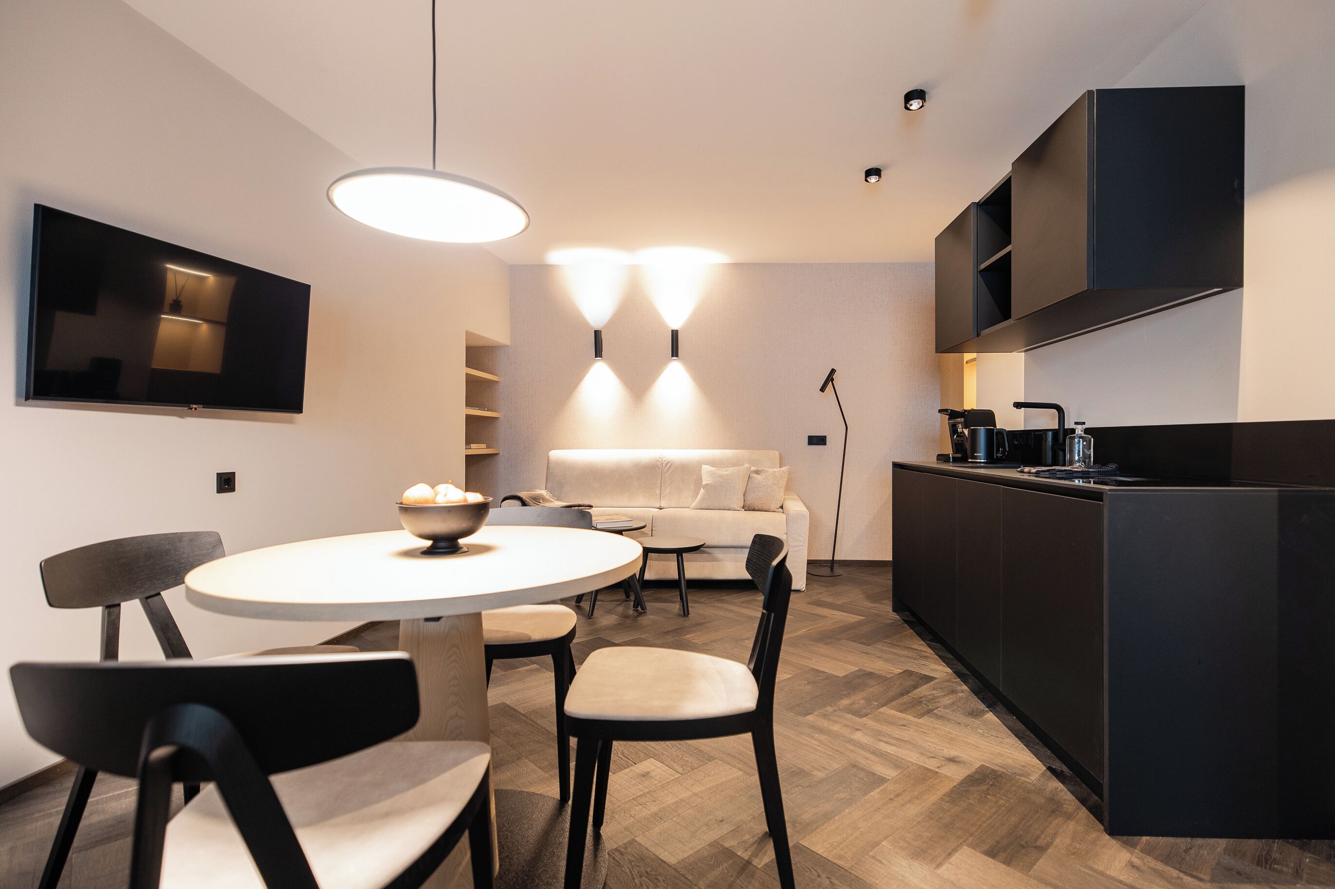 A modern kitchen with a dining area, featuring a round table, chairs, a sofa, and built-in appliances.