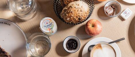 A breakfast table with croissants, an orange, a glass of water, a cup of coffee, and a plate with cheese and grapes.