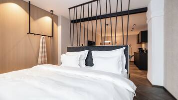 Una habitación de hotel moderna con una cama grande, cabecera de madera, una toalla colgada y vistas al área de la cocina.