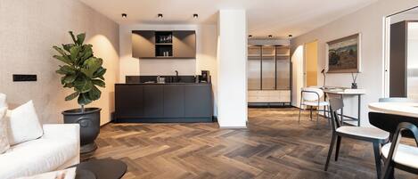 Un salon moderne avec un parquet en chevrons, un canapé blanc, une table basse noire et une grande plante en pot.