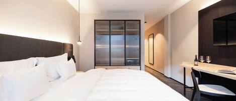 Una habitación de hotel moderna con una cama grande, un escritorio con dos sillas y vista a través de una puerta con vidrio esmerilado.