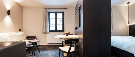 Una habitación de hotel moderna con una cama, un escritorio y una silla. Tiene una ventana con cortinas, un radiador y un aplique de pared.