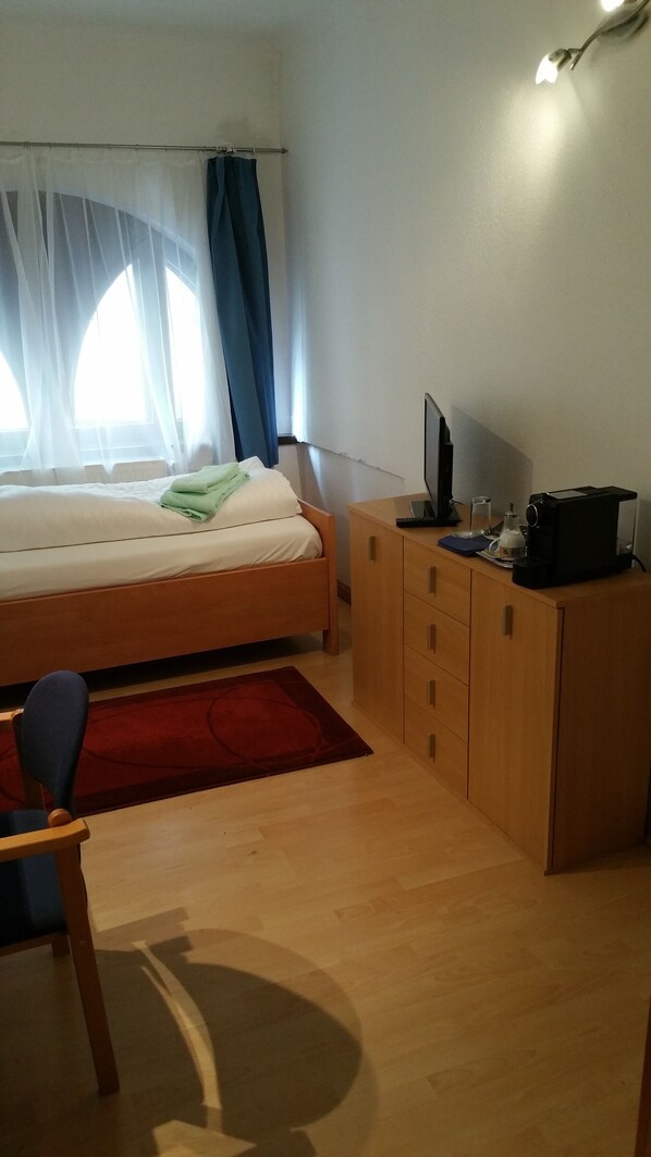 A bedroom with a bed, a wooden desk, a television, and a coffee machine. - Appartementhotel Marien-Hof (Vienna)