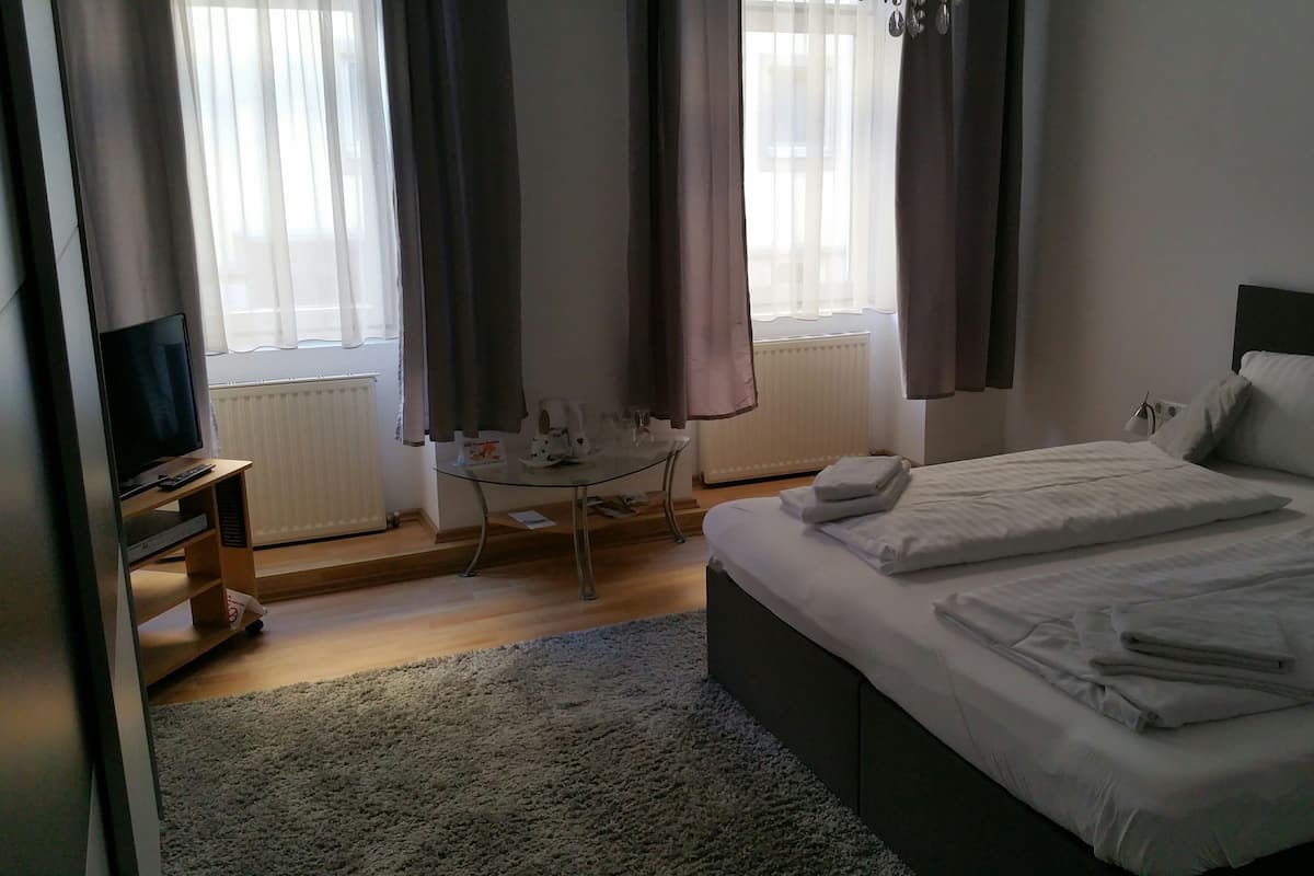 Ein Hotelzimmer mit Bett, Fernseher, einem kleinen Tisch und einem Fenster mit Vorhängen.