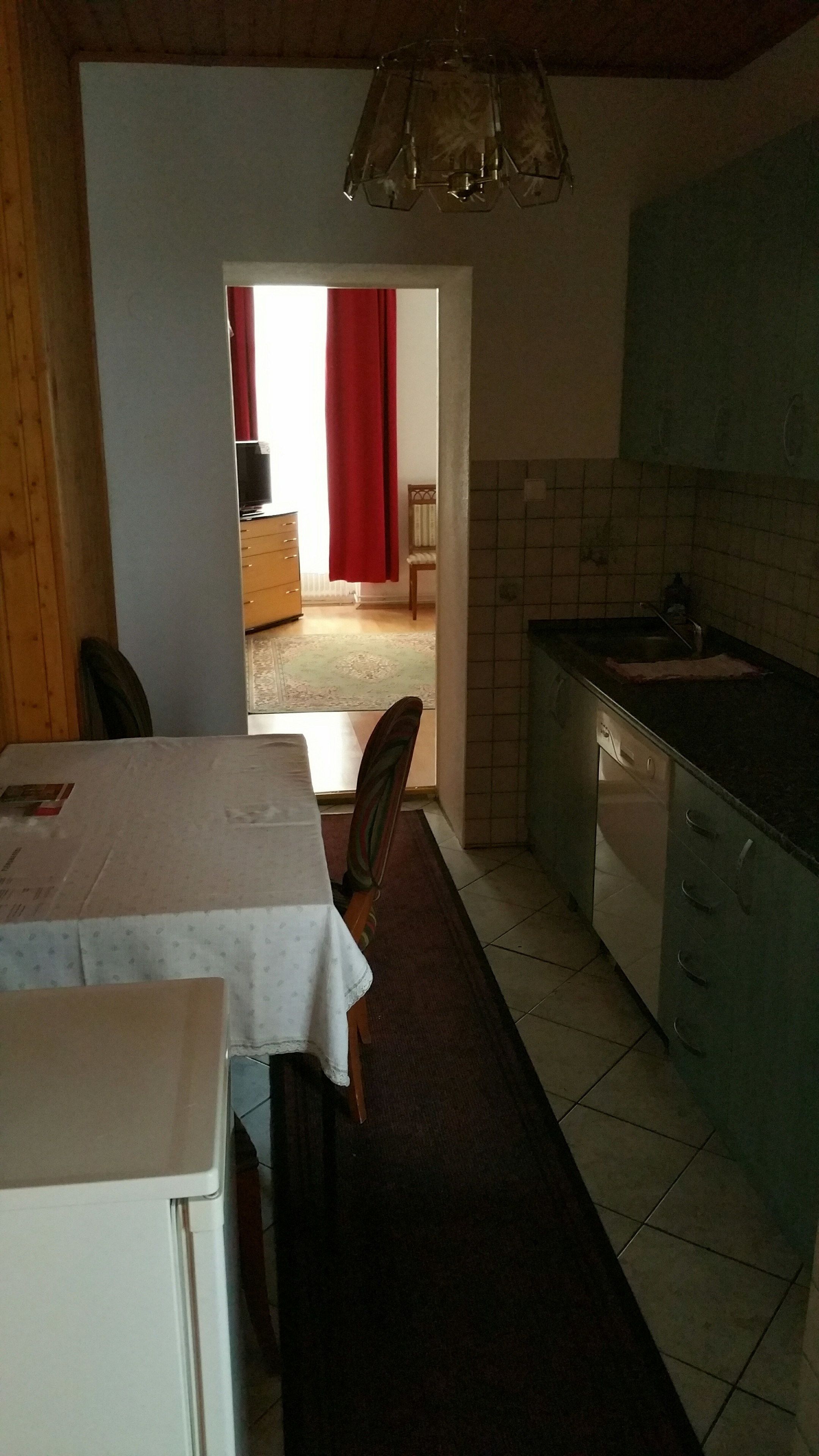 Une cuisine avec un coin repas, un plafond en bois et une vue sur une autre pièce, séparée par un rideau rouge.