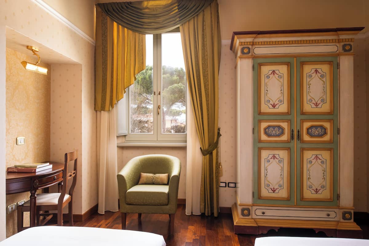 Une pièce comprenant un lit, un bureau avec des livres, une chaise, une armoire et une fenêtre avec des rideaux.