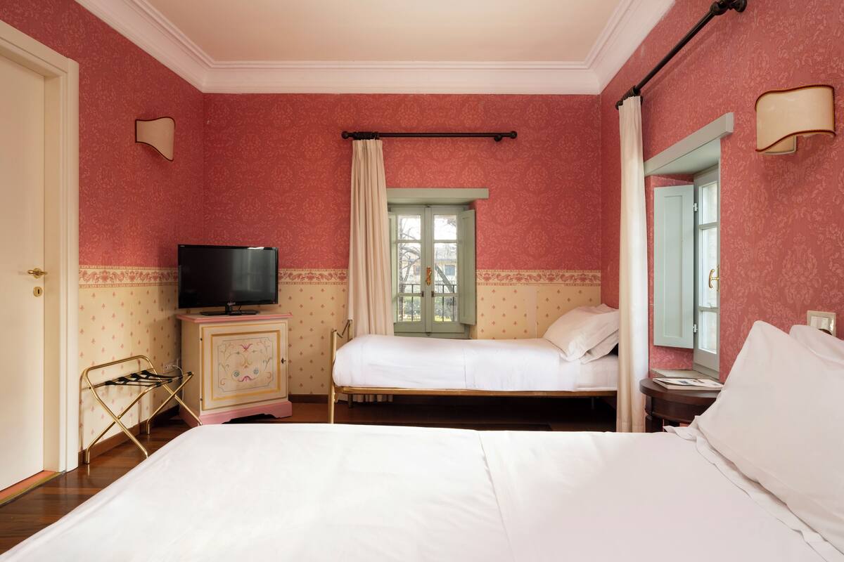 Une chambre d’hôtel avec un lit, une télévision, une commode et une fenêtre avec des rideaux.