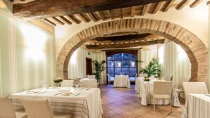 A restaurant with multiple tables, white tablecloths, wicker chairs, and a brick archway. - RELAIS PARCO DEI CAVALIERI ASSISI (Assisi)