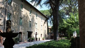 A stone building with multiple windows and a courtyard with potted plants and a statue. - RELAIS PARCO DEI CAVALIERI ASSISI (Assisi)