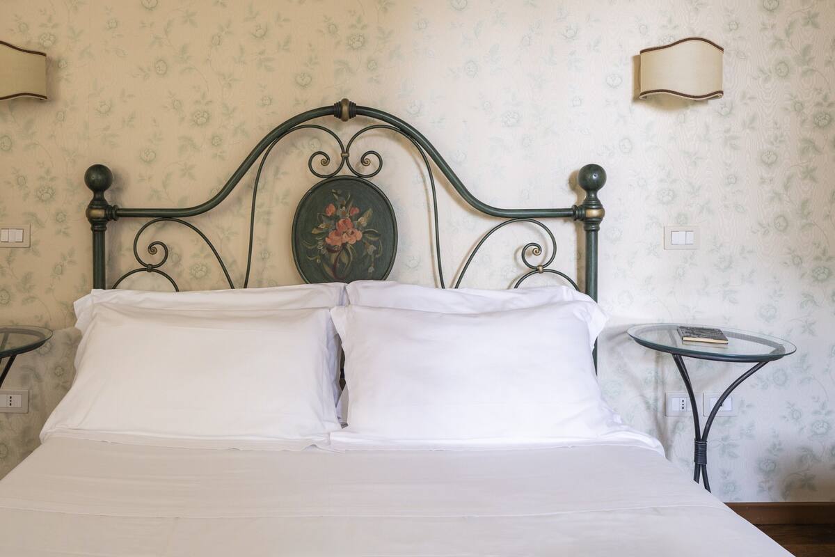 Un lit bien fait, avec du linge de lit blanc, un papier peint à motifs floraux et deux tables de chevet avec des lampes.