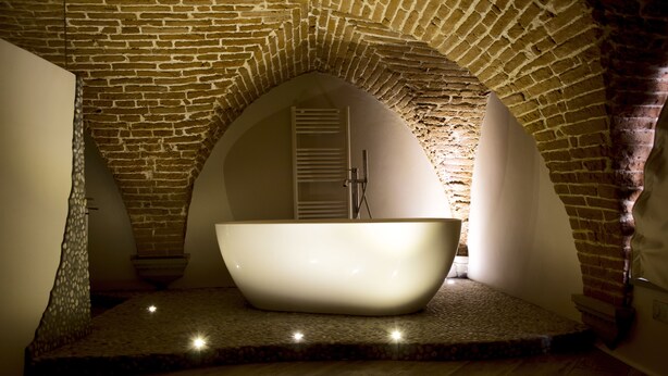 A modern bathroom with a freestanding bathtub, stone flooring, and brick arches. - N4U Guest House (Florence)