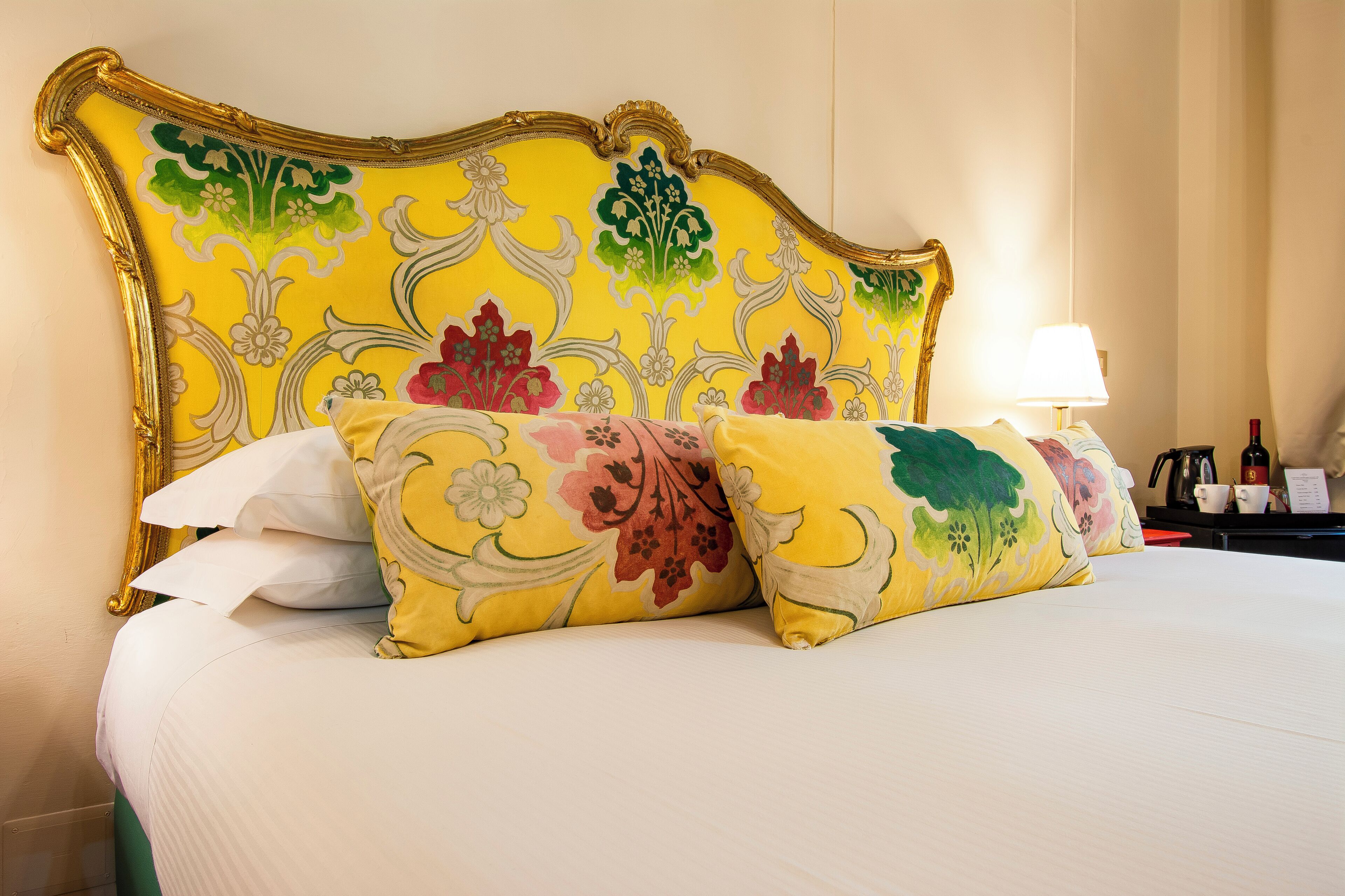 A bed with a yellow floral headboard, white bedding, and multiple pillows.
