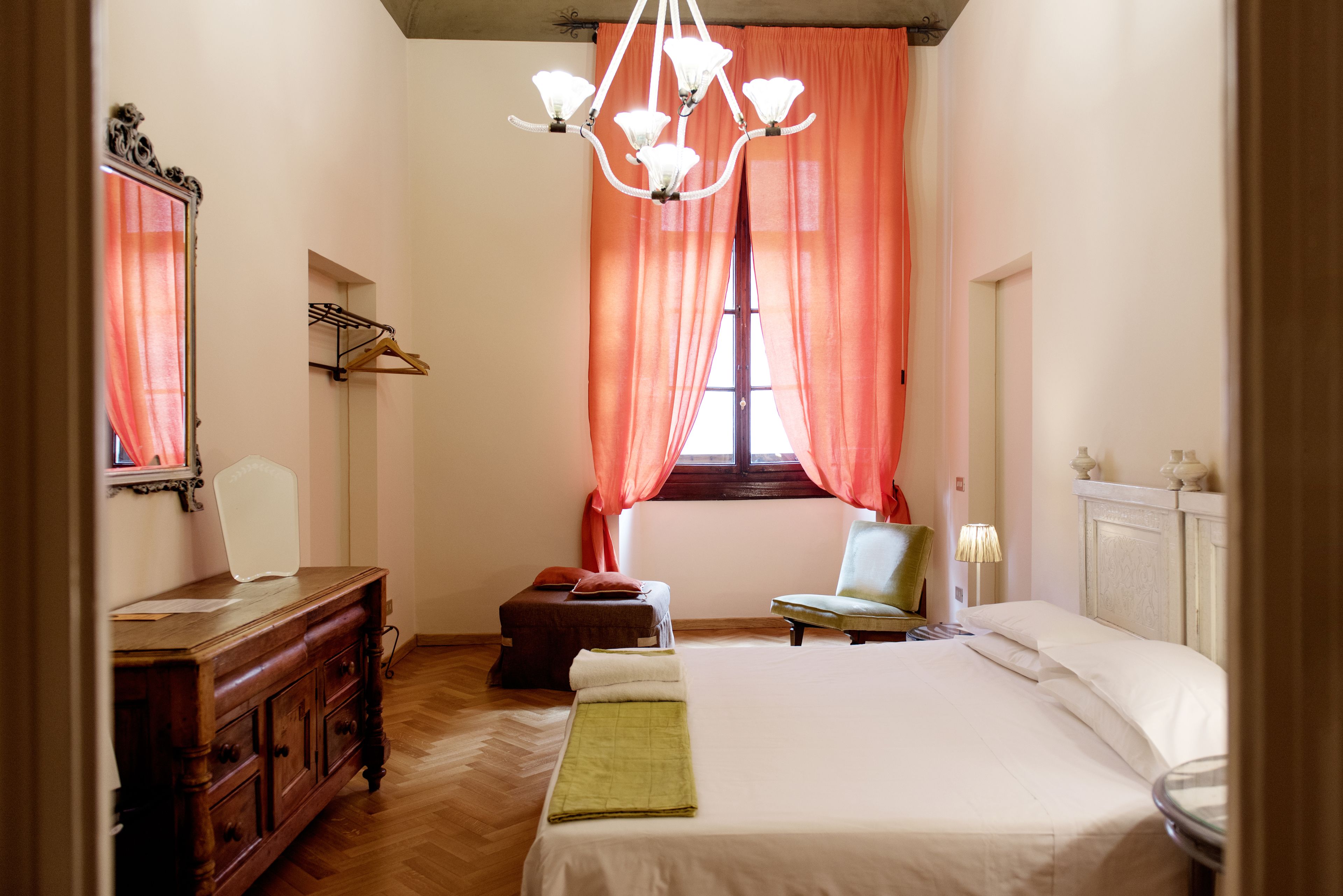 A bedroom with a bed, a wooden dresser, a chair, and a window with curtains.