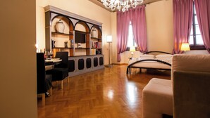 A hotel room with a wooden floor, a bed, a desk with a chair, a bookshelf, and a chandelier. - N4U Guest House (Florence)