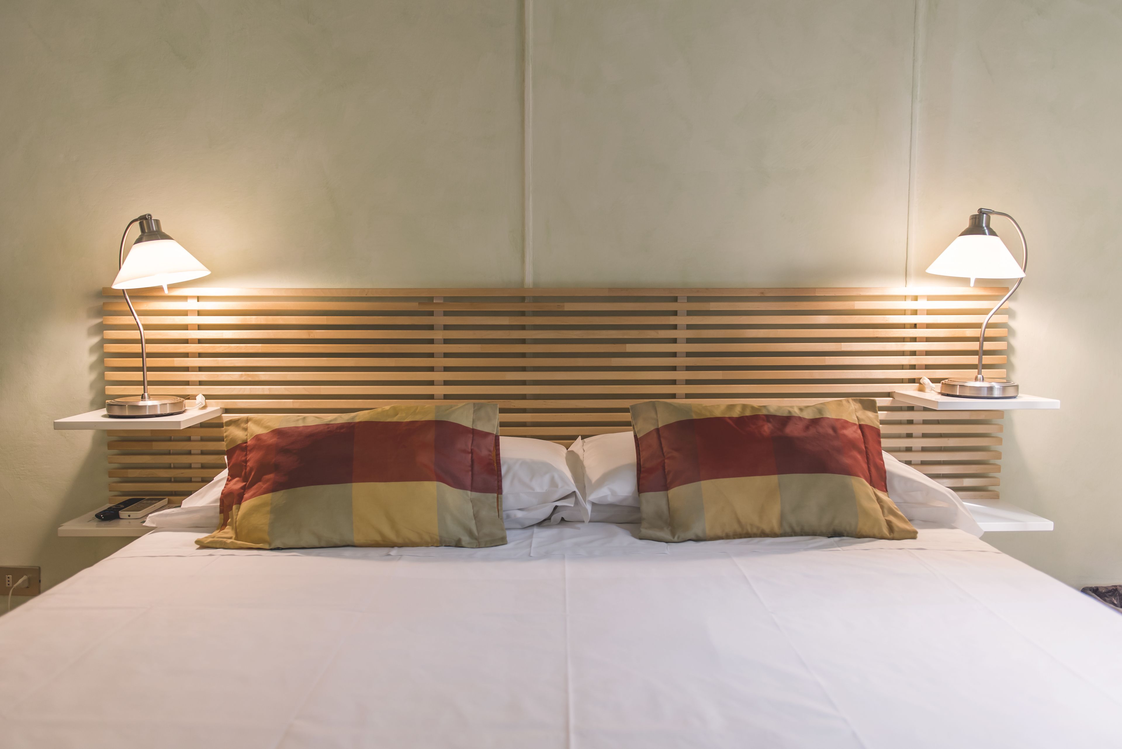 A neatly made bed with two pillows, a wooden headboard, and bedside lamps.