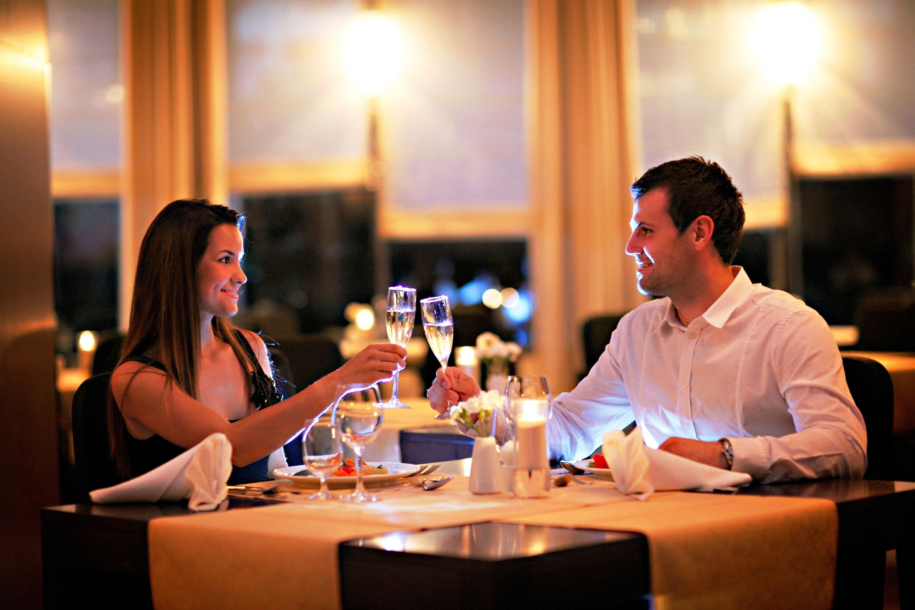 A couple dining at a table with wine glasses, a candle, and a vase of flowers.