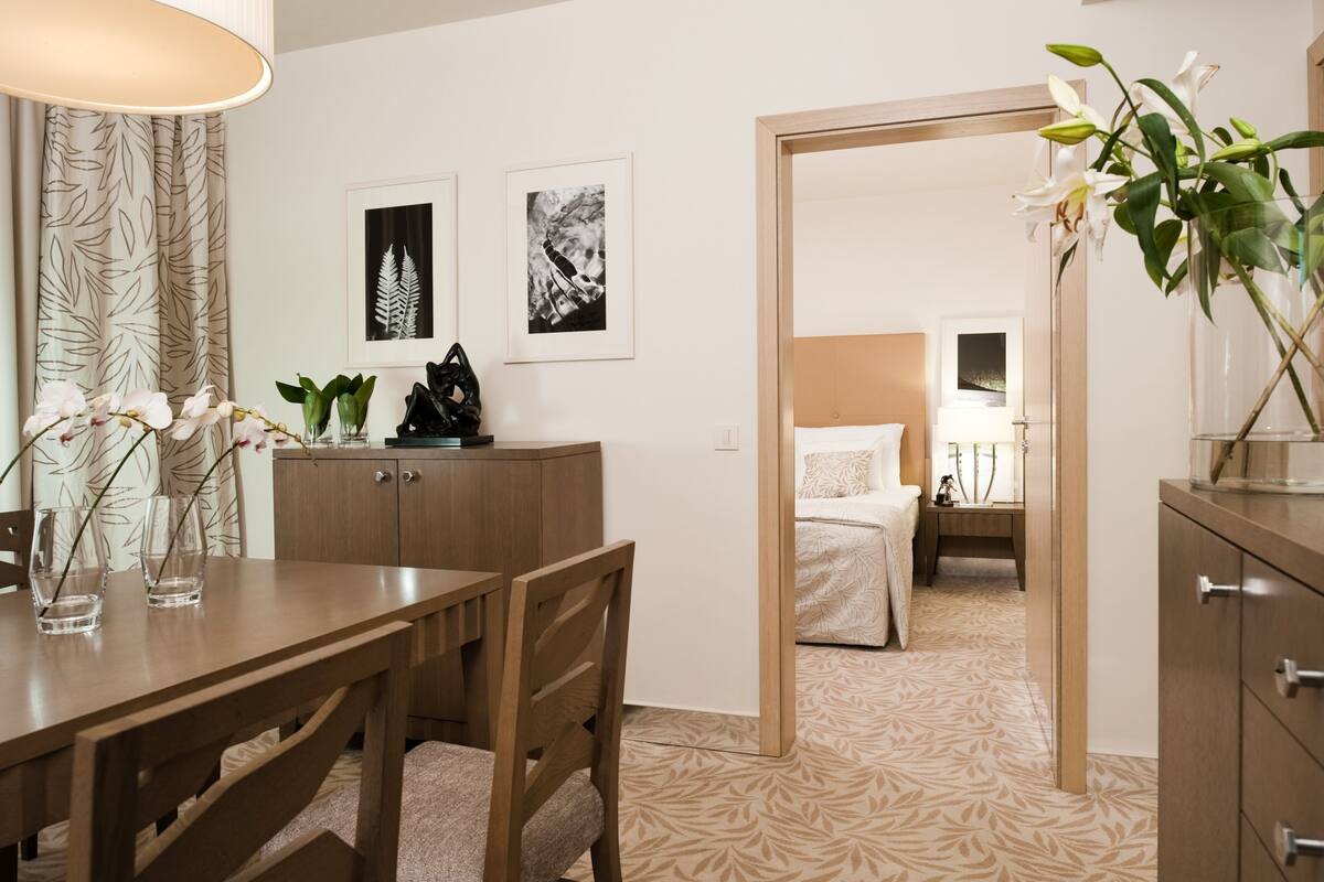 Une chambre d’hôtel avec un bureau en bois, un lit doté d’une tête de lit blanche, une table de chevet et une grande fenêtre.