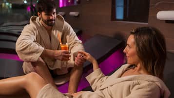 Ein Paar in einer Wellnessumgebung mit einer Massageliege und einem Glas Orangensaft.