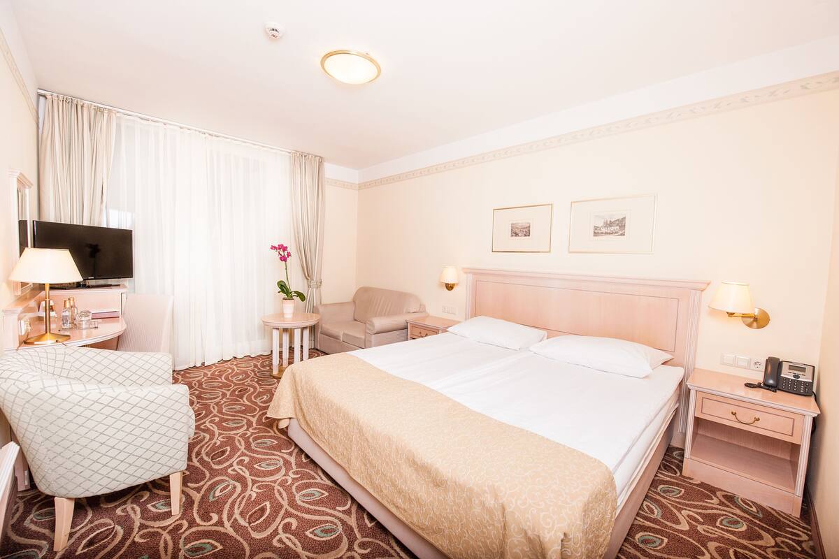 Une chambre d’hôtel avec un grand lit, un bureau avec une chaise, une télévision et deux tableaux encadrés au mur.