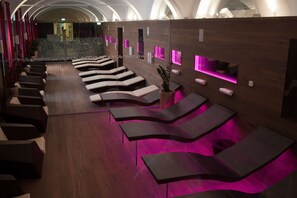 Un spa moderne doté de fauteuils inclinables aux lignes courbes et d’un éclairage d’ambiance rose.
