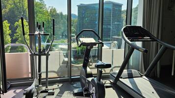 Un gimnasio con equipo de ejercicio y amplias ventanas que ofrecen vistas a un paisaje urbano.