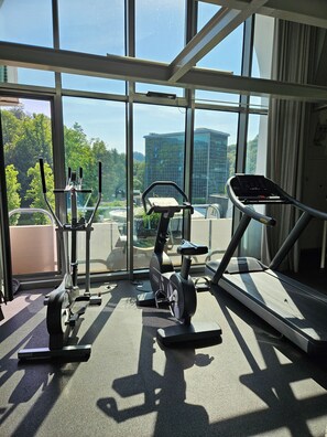 Un gimnasio con equipo de ejercicio y amplias ventanas que ofrecen vistas a un paisaje urbano.