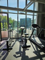 Un gimnasio con equipo de ejercicio y amplias ventanas que ofrecen vistas a un paisaje urbano.