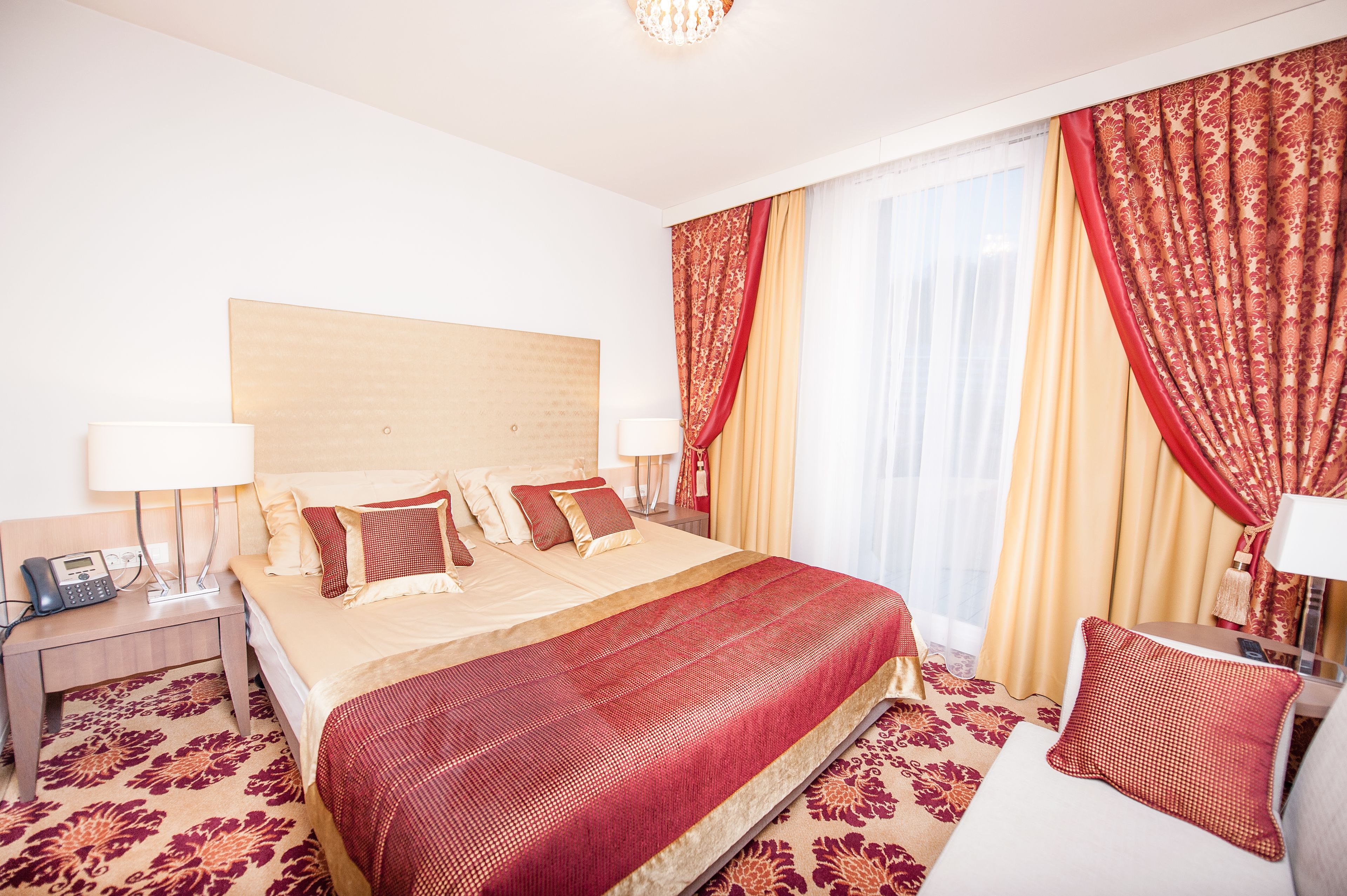 Una habitación de hotel con una cama grande, dos mesitas de noche y una zona de estar con una silla y una lámpara.