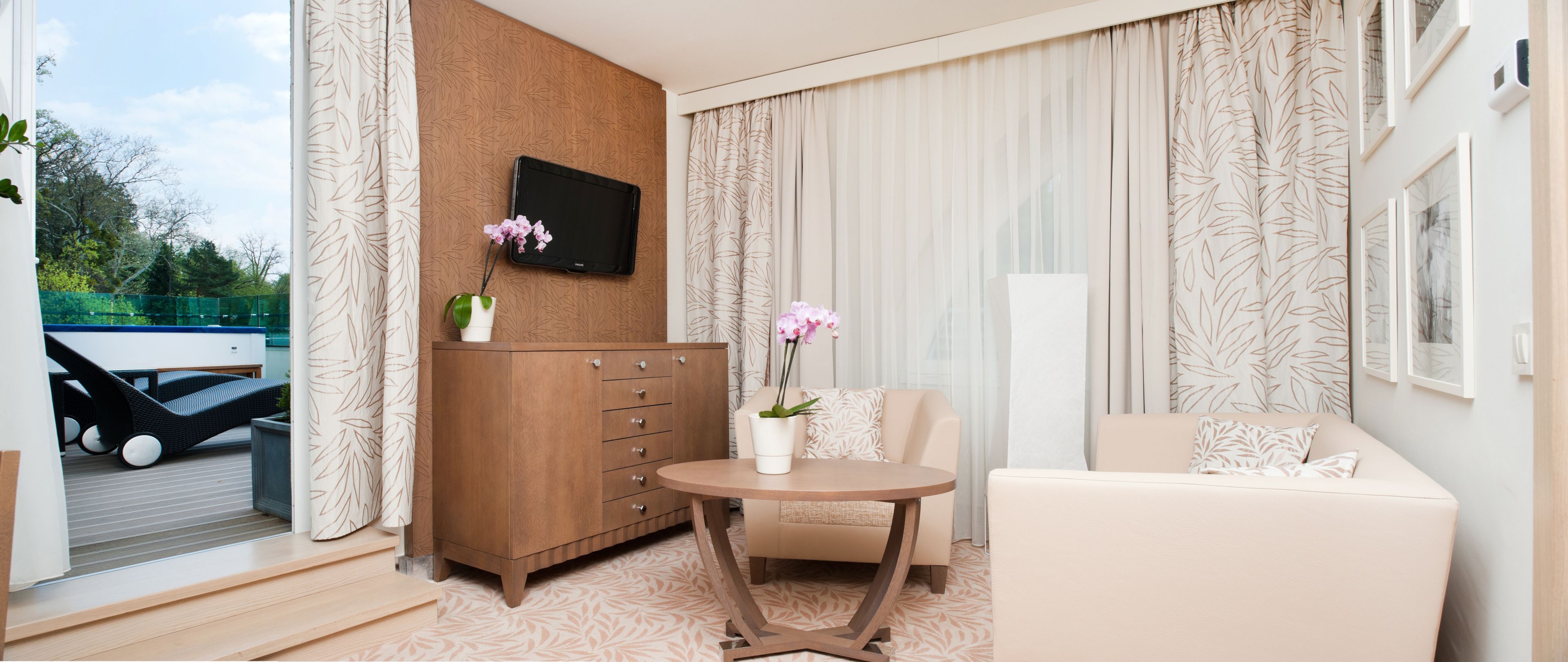 A modern hotel room with a sofa, a small table, a wooden cabinet, and a TV mounted on the wall.