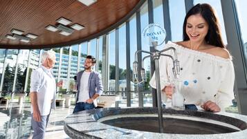 A modern indoor setting with a large water feature, a logo on the wall, and a glass railing.