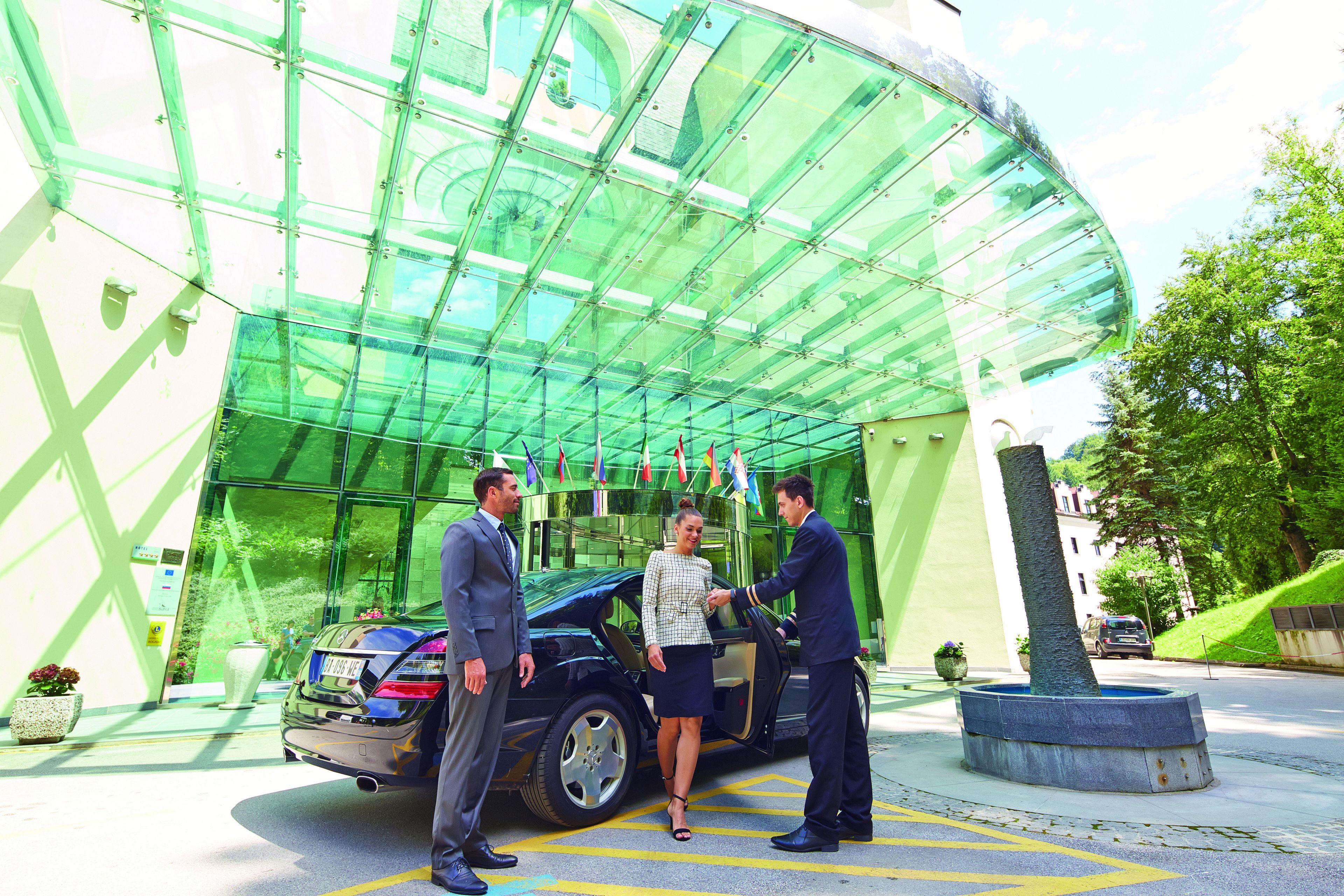 A modern building with a glass facade, a car parked in front, and a tree in a planter.