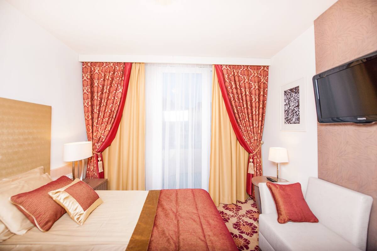 Une chambre d’hôtel avec deux lits, un canapé, une télévision et une fenêtre avec des rideaux.