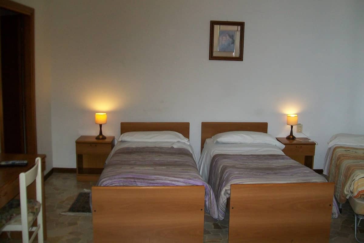 A room with two wooden beds, each with a nightstand and a lamp. There is a framed picture on the wall.