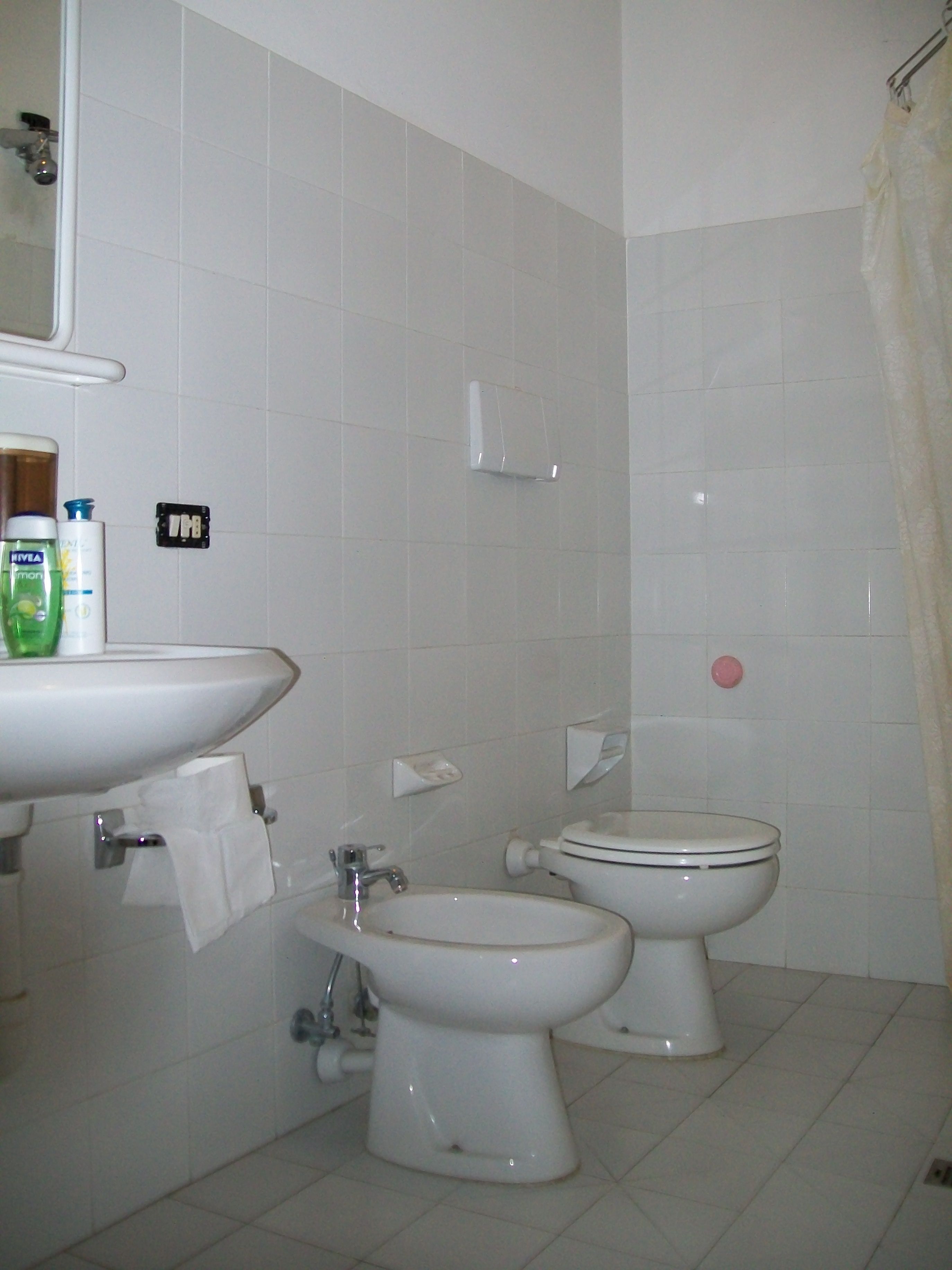 A bathroom with a sink, two toilets, and a shower curtain.