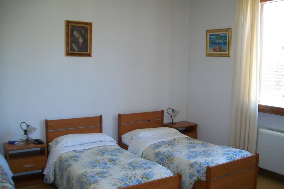 A room with two wooden beds, each with a nightstand and a lamp. There are two framed pictures on the walls.