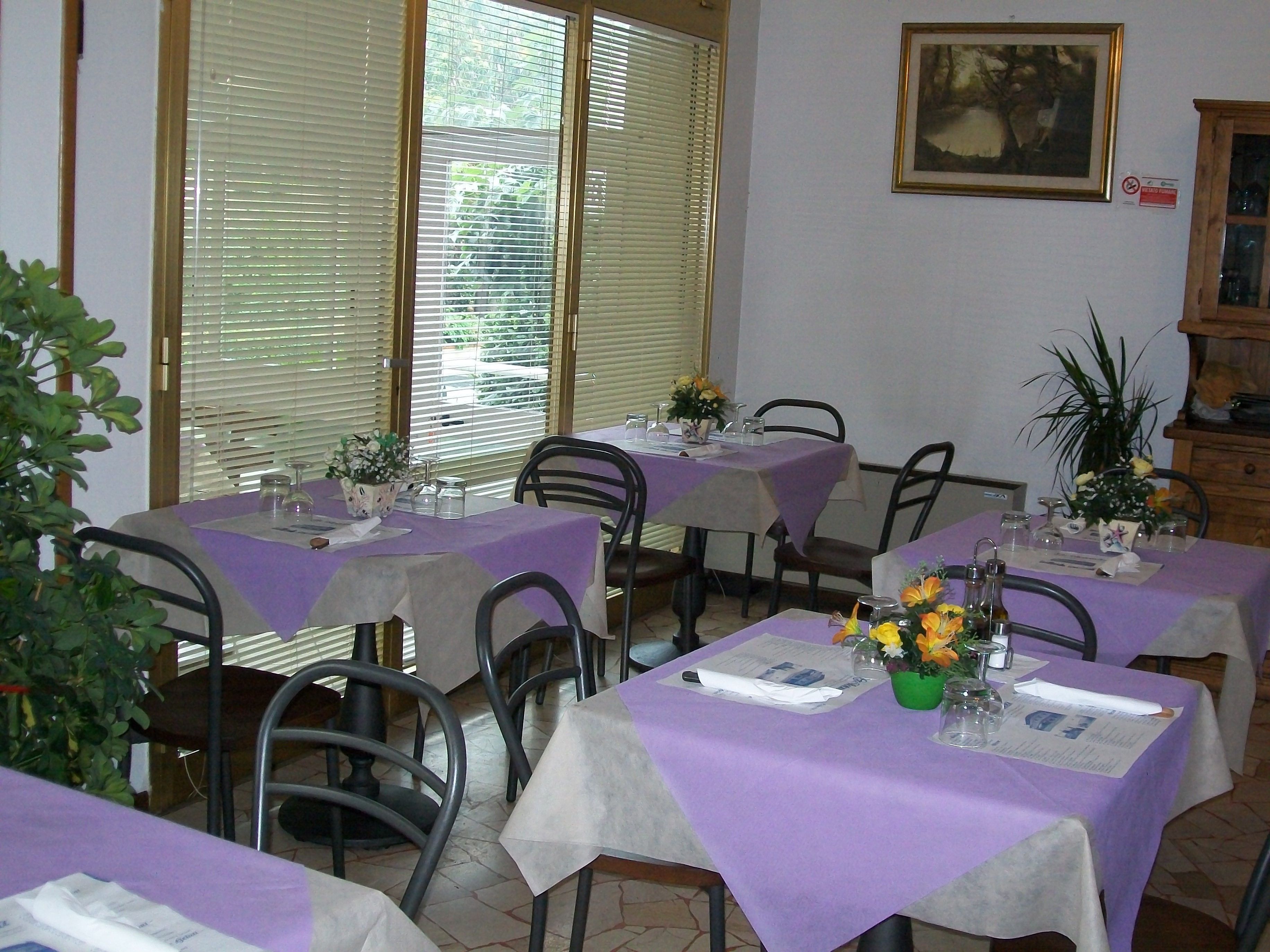 A dining area with tables covered in purple tablecloths, chairs, and potted plants.