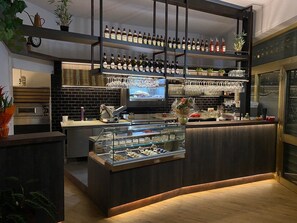 A modern bar area with shelves of bottles, a display case with snacks, and a television screen. - Locanda la Rotonda (Montale)
