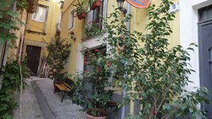 Un callejón estrecho con un edificio amarillo, una banca y plantas en macetas.
