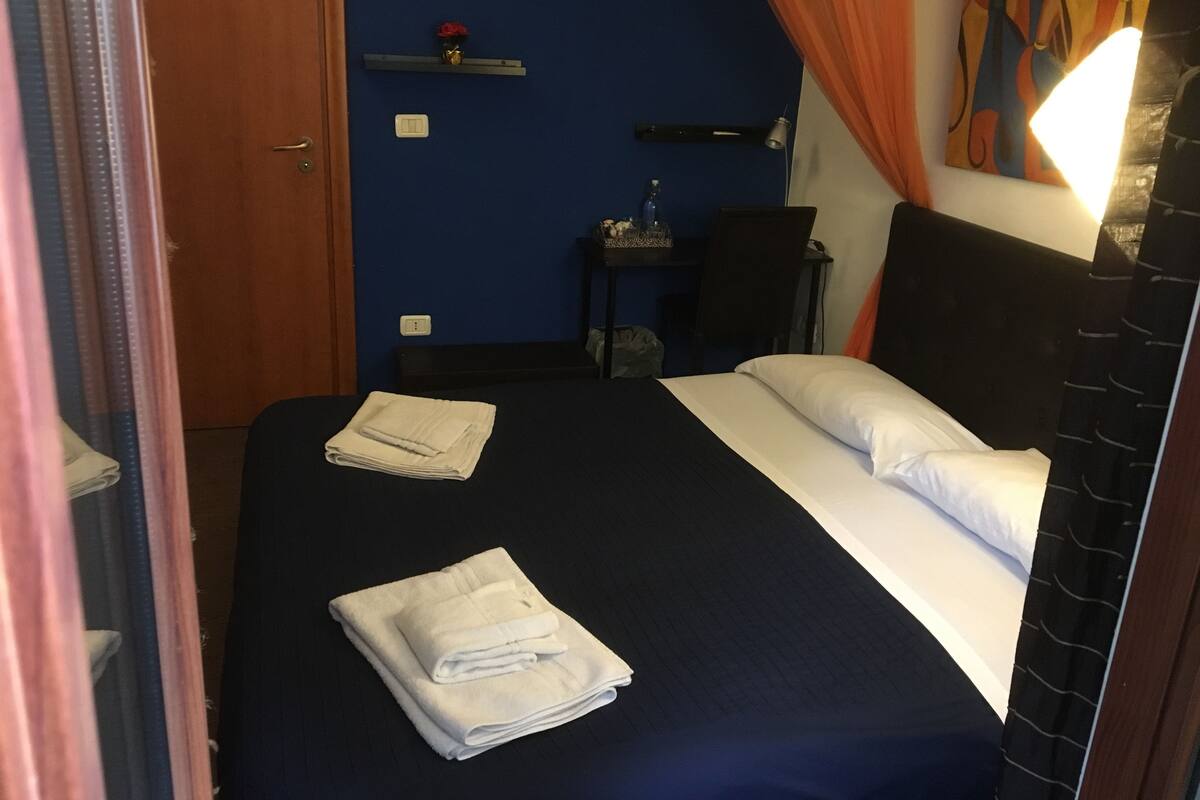 A hotel room with a bed, a desk, a chair, and a nightstand.