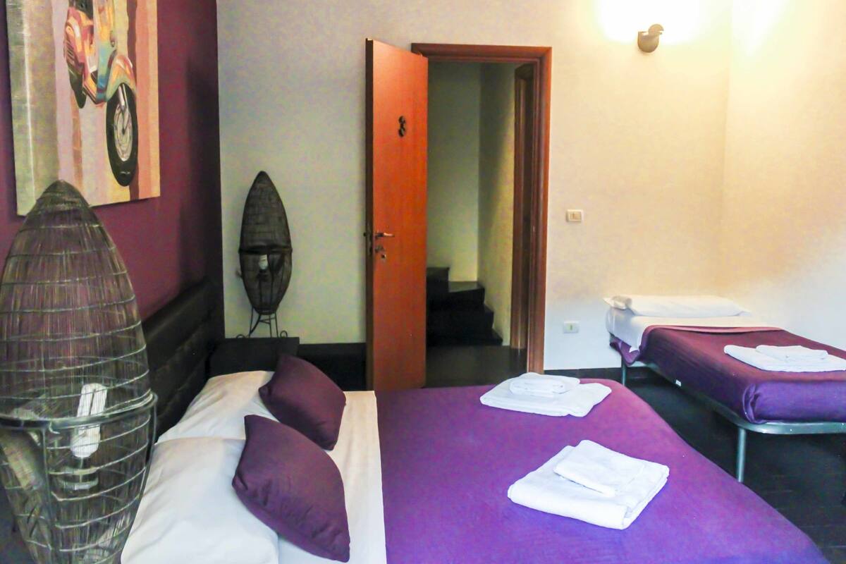 A hotel room with two beds, purple bedding, a clear view of the hallway, and a door leading to another room.