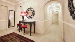 A hallway with a red upholstered chair, a table with a red lamp, and a decorative mirror. - Residenza Maglioni al Battistero (Florence)